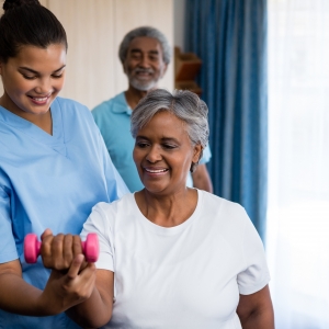 Nurse guiding senior woman in lifting dumbbell at retirement home